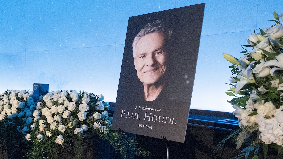 Une affiche qui montre Paul Houde souriant est entourée de bouquets de roses lors de la chapelle ardente.