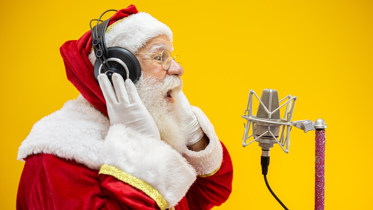Un homme portant un costume de père Noël chante devant un micro de style studio.