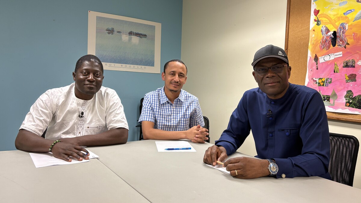 Trois hommes dans une salle de conférence. 