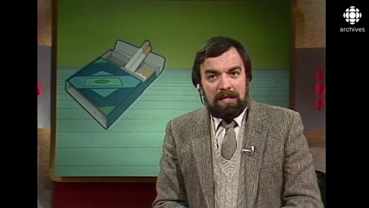 Le présentateur est devant une illustration d'un paquet de cigarettes. 