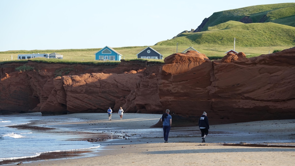 Des gens marchent sur la plage de la Dune-du-Sud au pied de falaises de grès rouge.