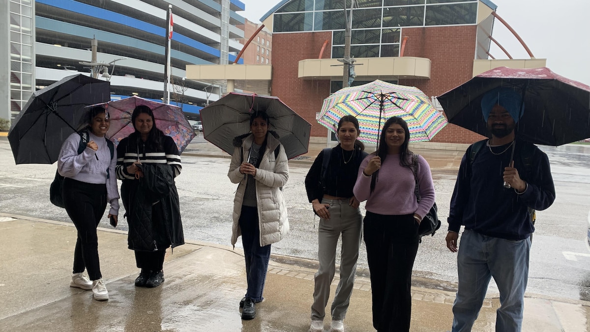 Des jeunes se protègent de la pluie sous leur parapluie au centre-ville de Windsor.