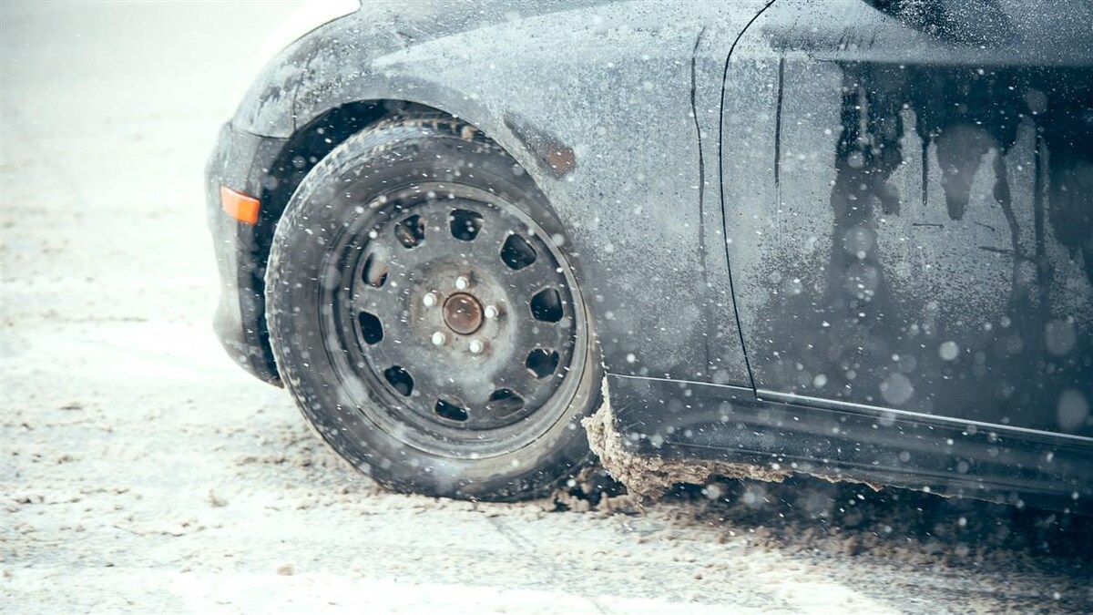 Gros plan sur le côté d'une voiture et un pneu qui roule sur une chaussée enneigée durant une tempête de neige.