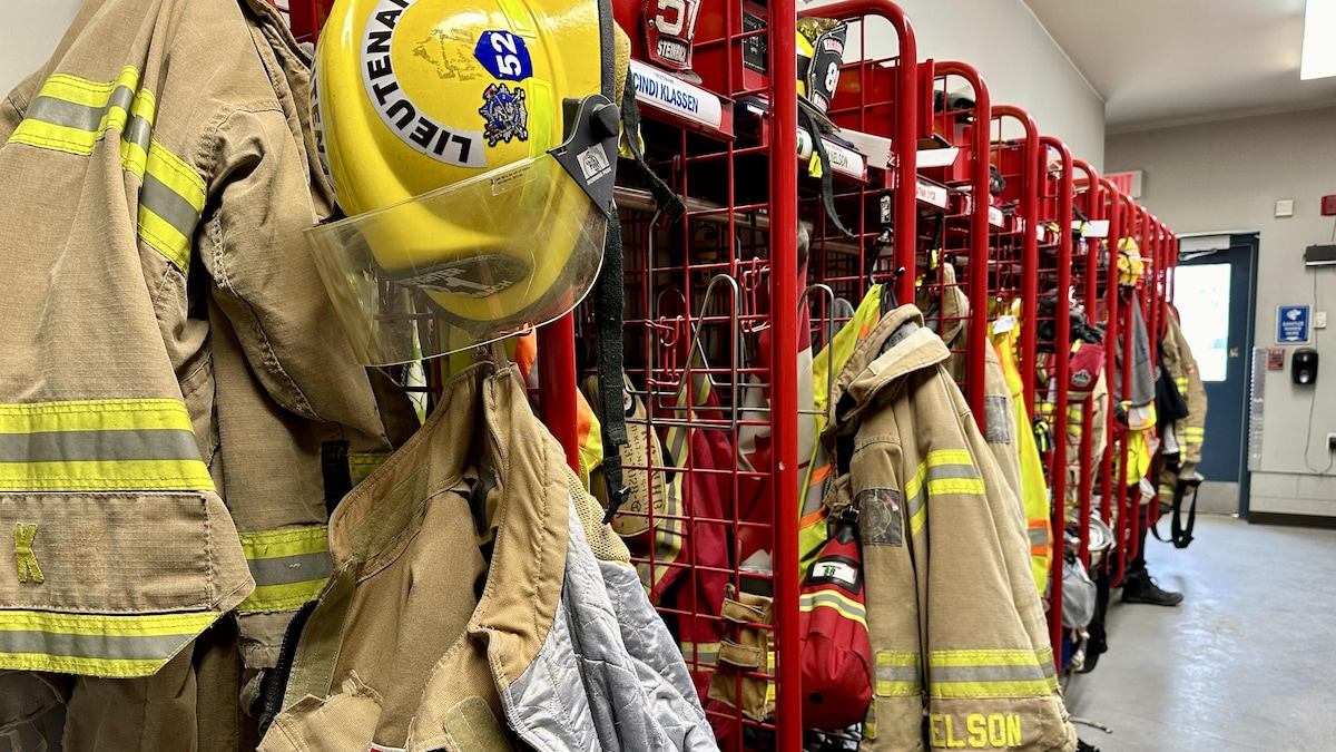 Des manteaux et des casques de pompiers sont accrochés dans des casiers métalliques rouges. 