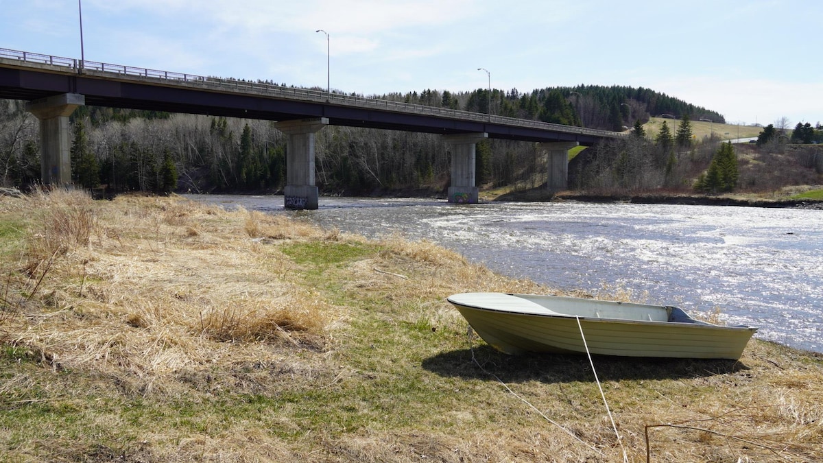 Une chaloupe repose sur la berge de la rivière; le pont figure à l'arrière-plan.
