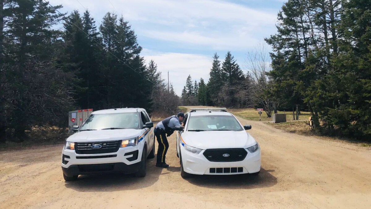 Un agent discute avec un collègue qui se trouve à bord d'une voiture de la Gendarmerie royale du Canada. Cette voiture et un autre véhicule bloquent la route.