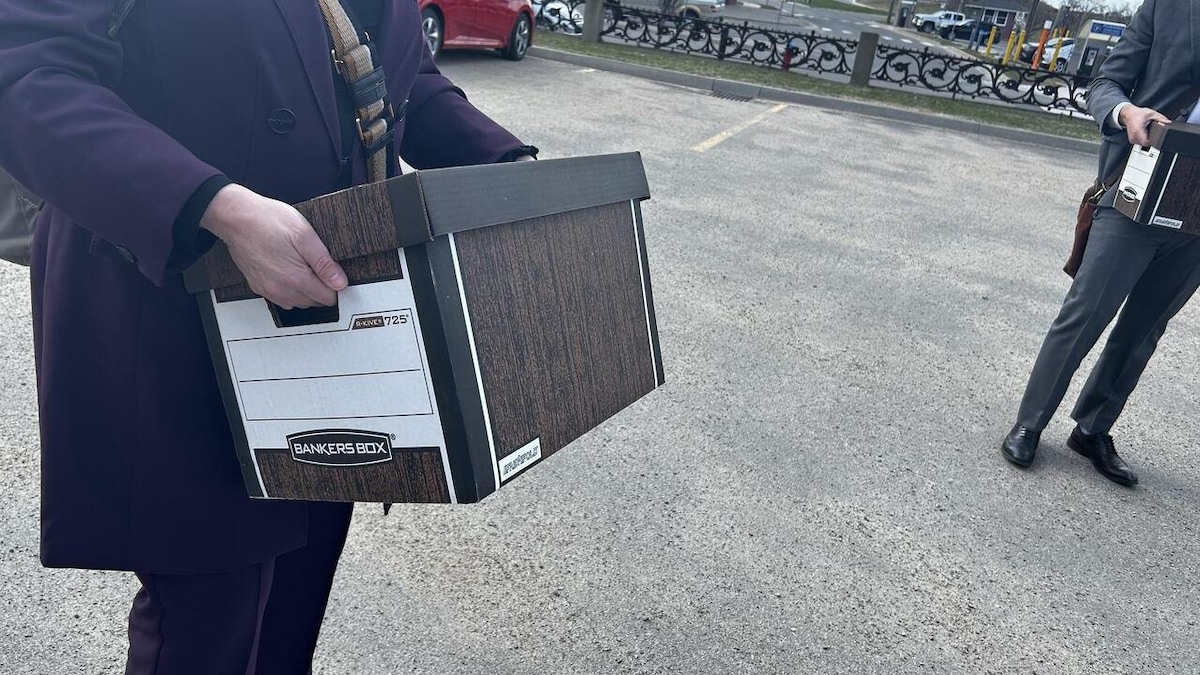 Des avocats à l'extérieur du tribunal transportent des boîtes.