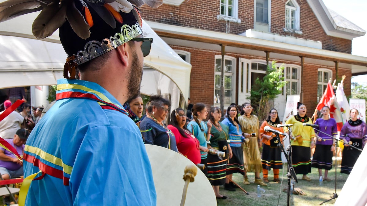 Un homme en habits traditionnels abénakis chante avec un tambour à la main. 