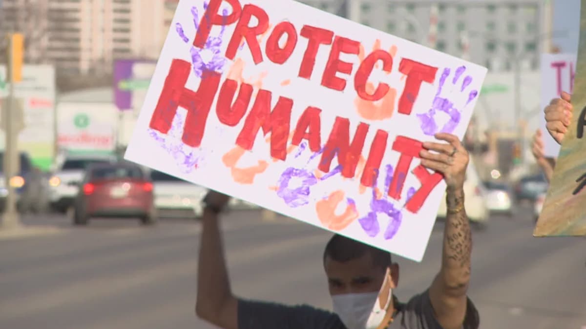 Une personne dans la rue et portant un masque tient une pancarte sur laquelle on peut lire « Protégez l'humanité ».