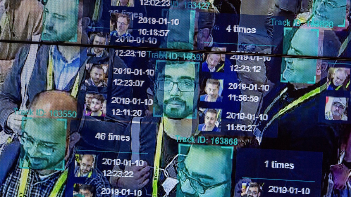 Capture d'écran d'un moniteur de caméra utilisant un logiciel de reconnaissance faciale. On voit le visage de plusieurs hommes être analysés.
