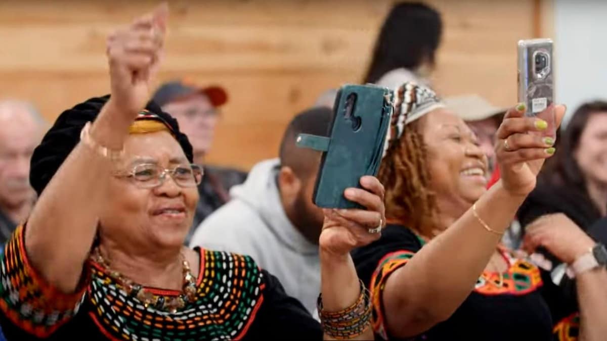 Deux femmes qui portent l'habit traditionnel d'un pays africain sourient en tenant un téléphone dans la main. 