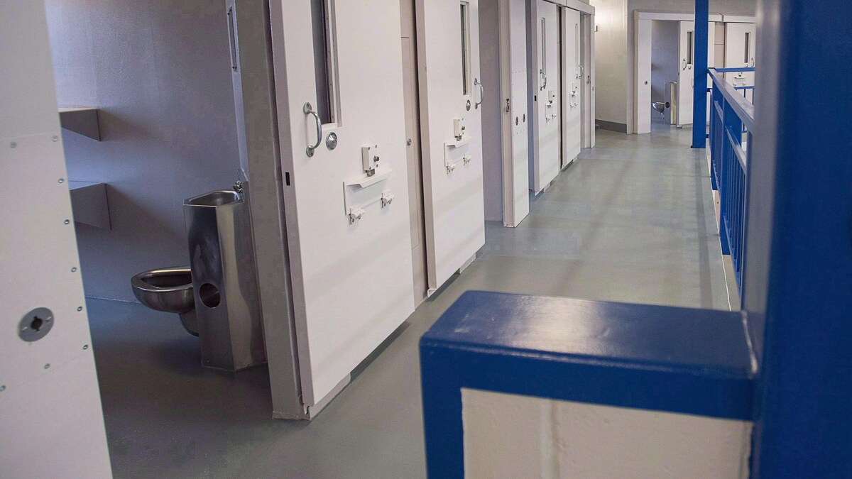 Corridor de la prison et vue sur une toilette dans une cellule.