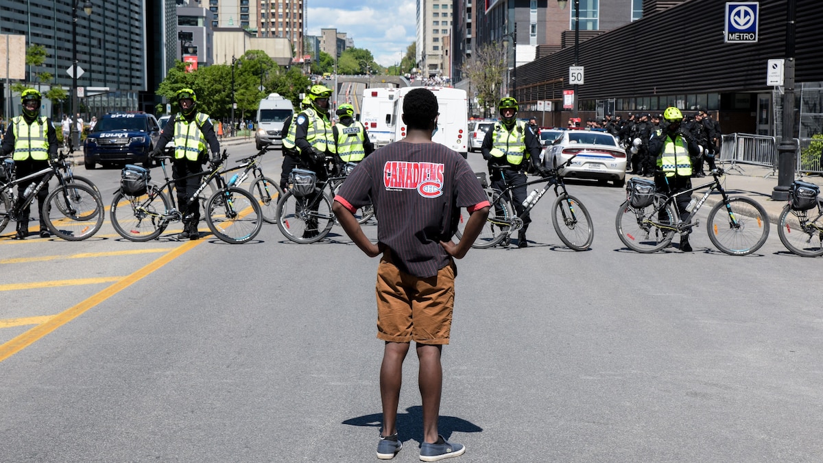 Un homme, les mains sur les hanches, se tient debout en étant tourné vers des policiers à bicyclette.
