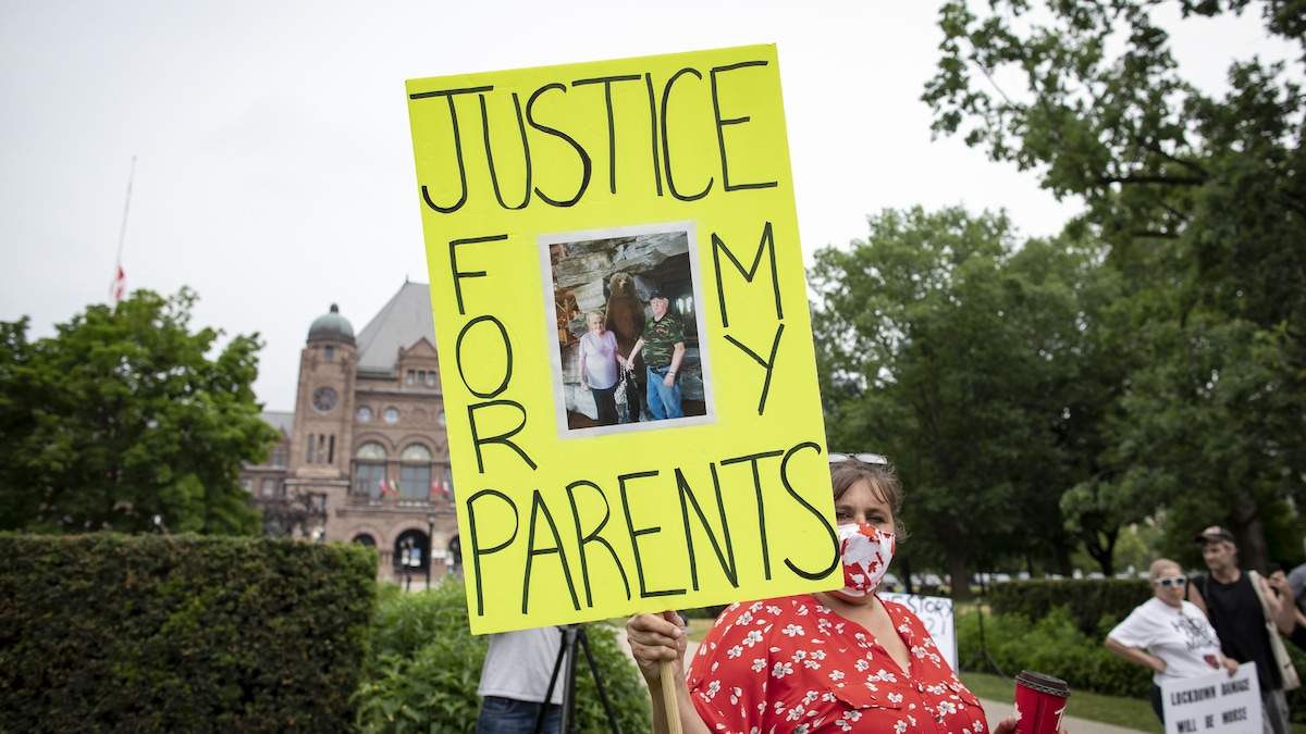 Une femme tient un pancarte sur laquelle il y a une photo de ses parents et l'inscription "Justice for my parents". Derrière elle, l'Assemblée législative, au loin. 