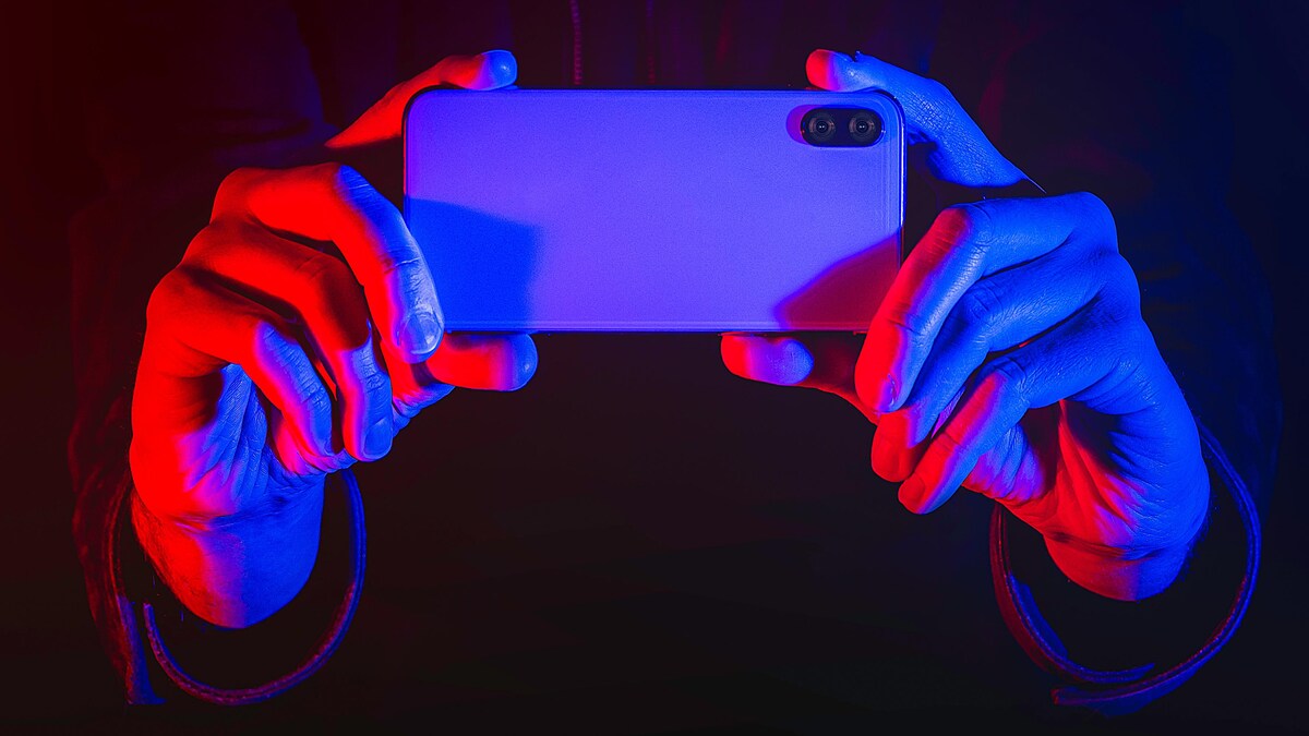 Deux mains tiennent un téléphone éclairées par des lumières rouges et bleues qui rappellent les gyrophares d'une voiture de police.