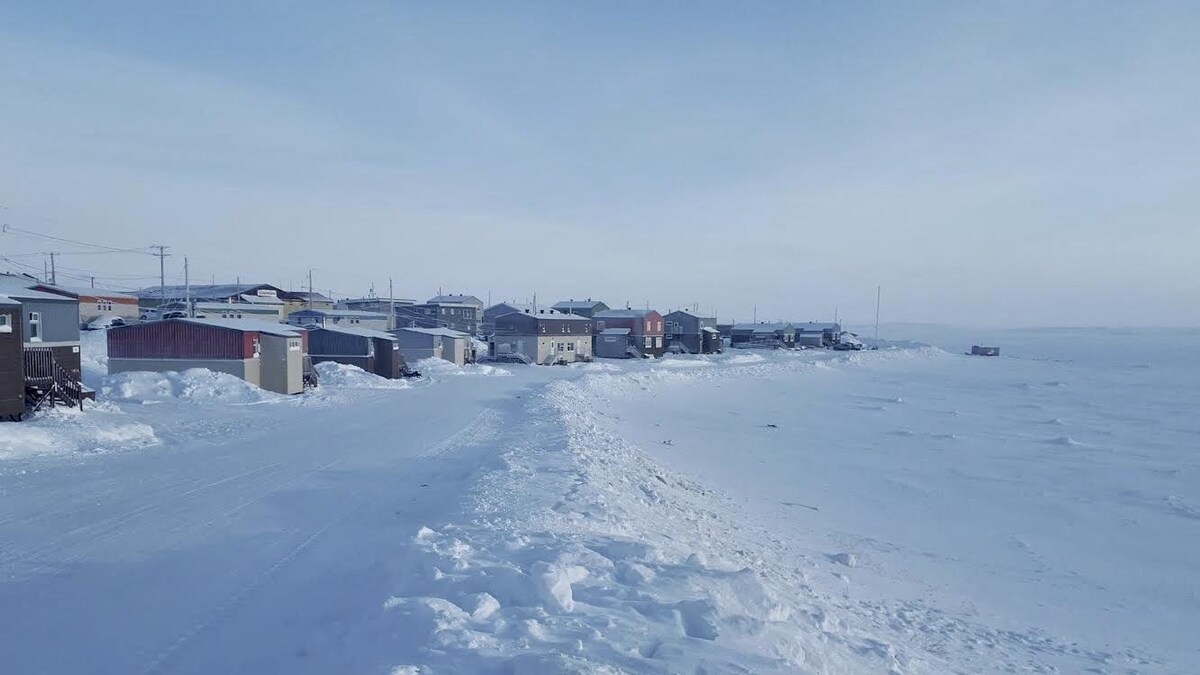Des maisons sont situées en face de la Baie d'Hudson. Le sol est enneigé. 