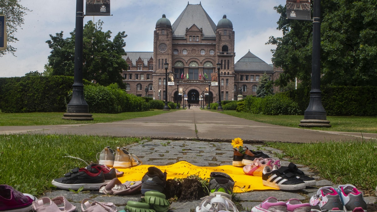 Des chaussures d'enfants reposent au pied de la statue de Sir John A. MacDonald, qui se trouve sur le terrain de l'Assemblée législative de l'Ontario à Queen's Park, à Toronto, le vendredi 18 juin 2021.