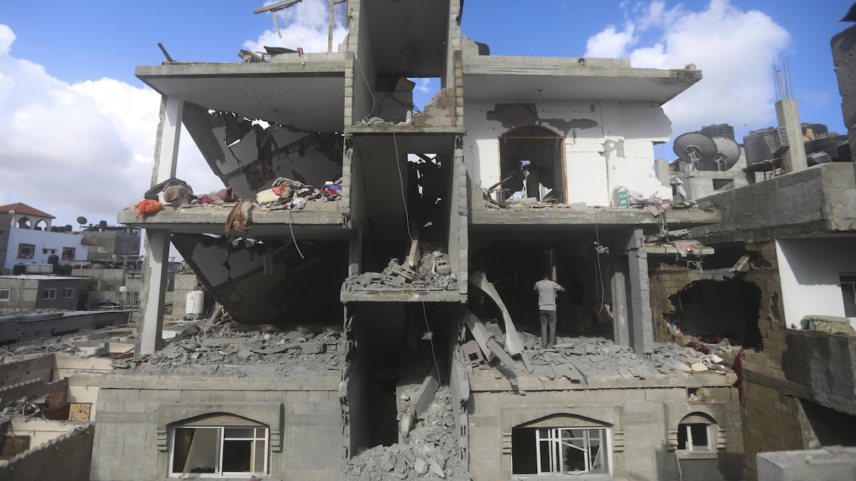 Des Palestiniens se tiennent debout dans un immeuble dont la façade et une partie des murs ont complètement été détruits.