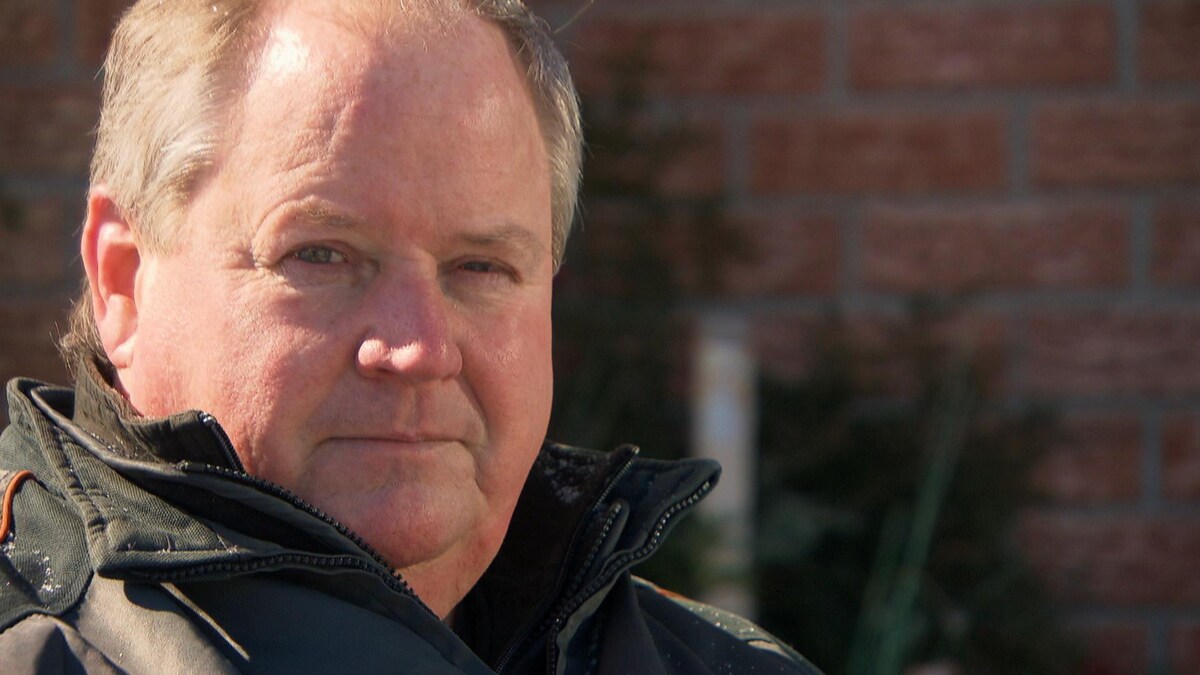 Portrait d'un homme avec un manteau d'hiver qui regarde la caméra devant un mur de briques.