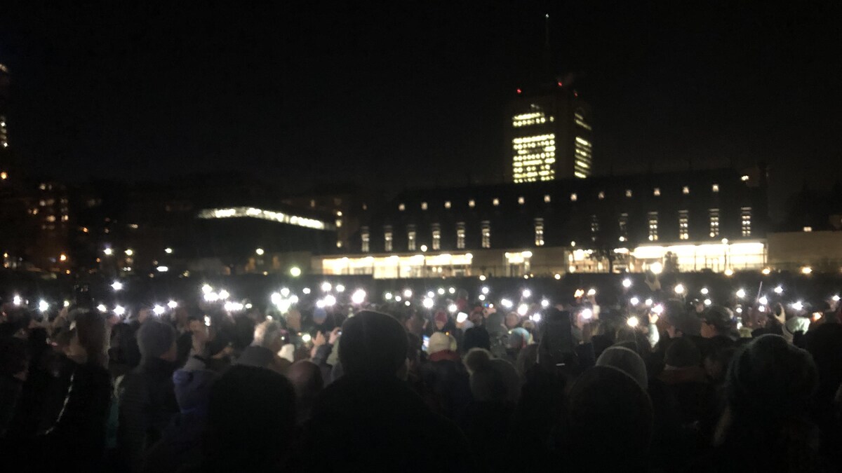 Des centaines de personnes dans le noir tenant chacun une lumière dans leurs mains sur les plaines d'Abraham devant le complexe G.