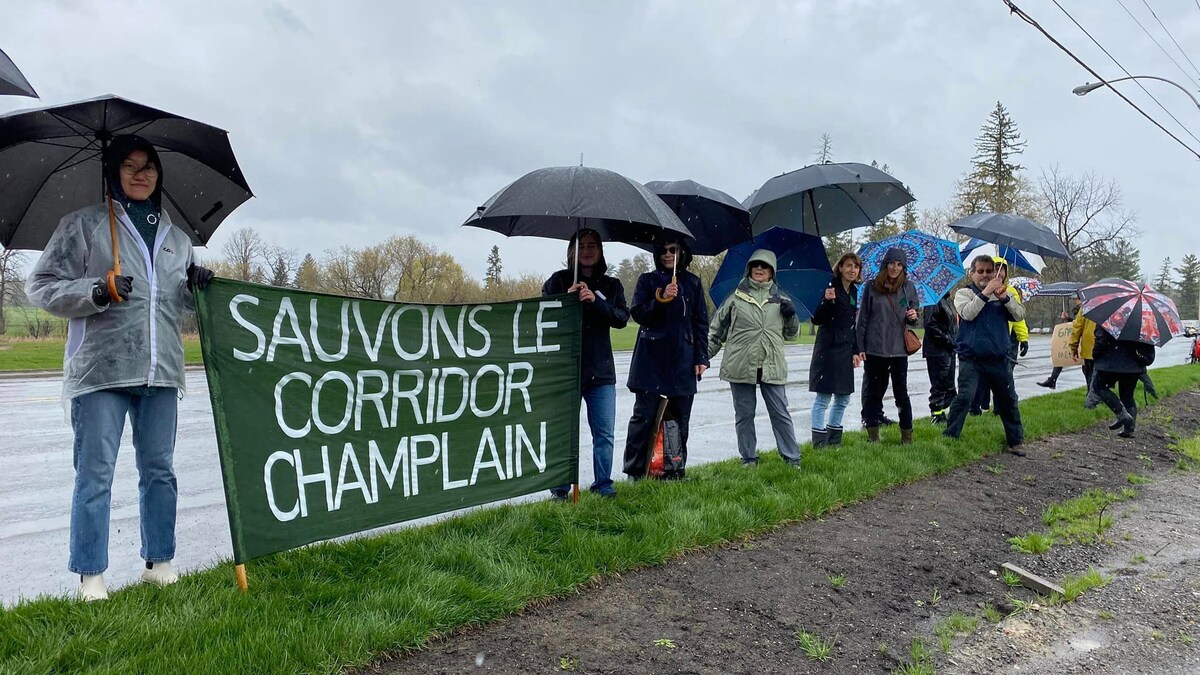 Des personnes sous la pluie tiennent une banderole sur laquelle il est écrit « Sauvons le corridor Champlain ».