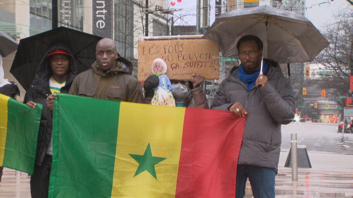 Emile Nioke, Papa N'Diongue et Mamadou Ba devant un drapeau aux couleurs de leur pays d'origine, le Sénégal, à Vancouver, le 11 février 2024.