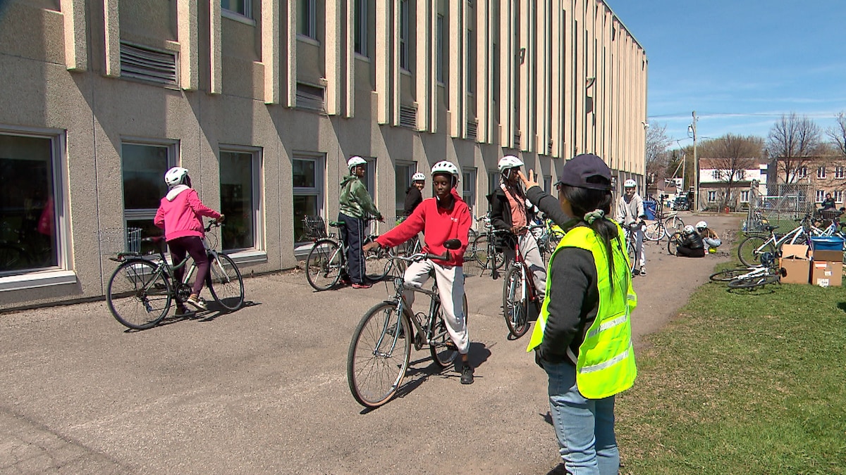 Au premier plan, une femme avec un dossard fait un signe à une jeune fille sur un vélo. Derrière, d'autres filles sont à vélo et attendent leur tour.