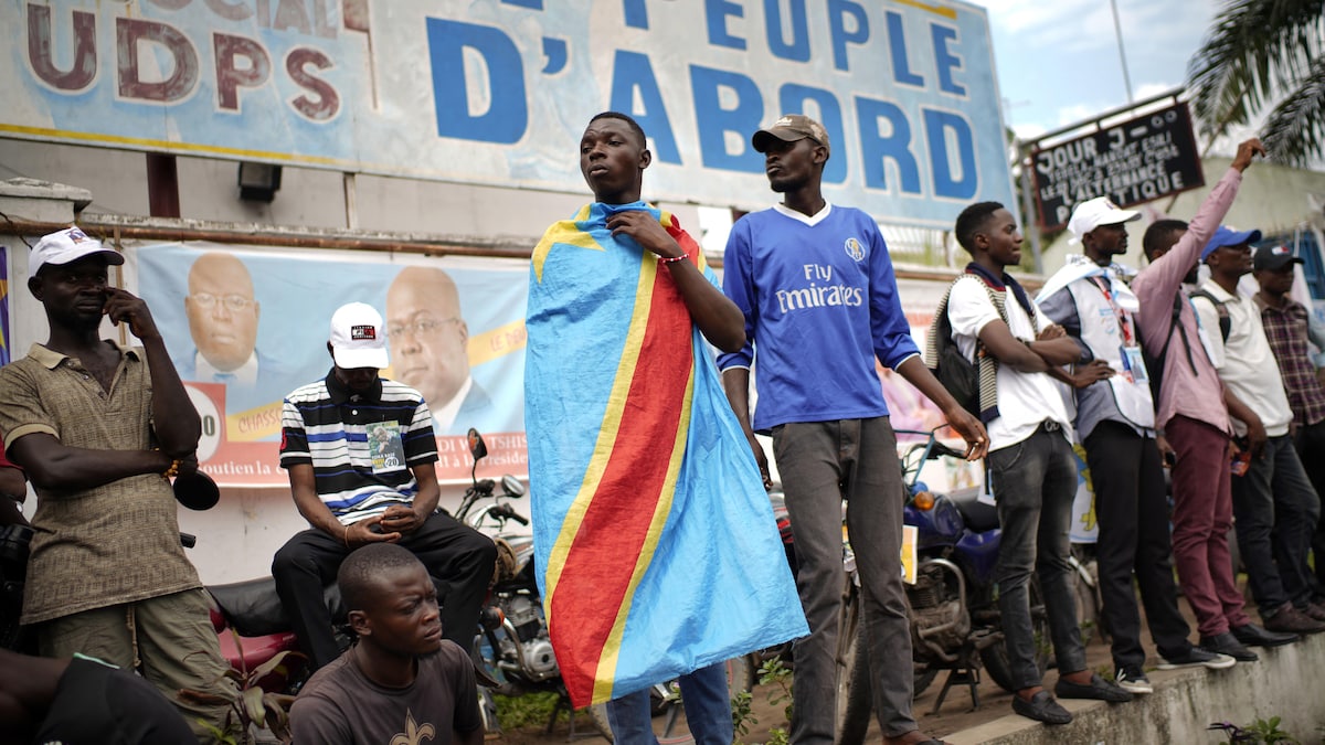 Des partisans attendent leur candidat. Un homme porte le drapeau de la République démocratique du Congo.