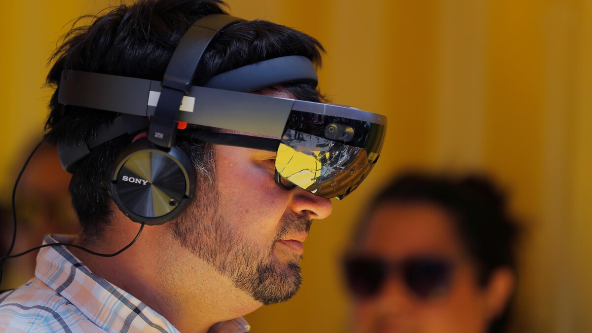Une photo montrant un homme portant un masque de réalité mixte Hololens, qui ressemble à de grosses lunettes de ski, et un casque d'écoute.