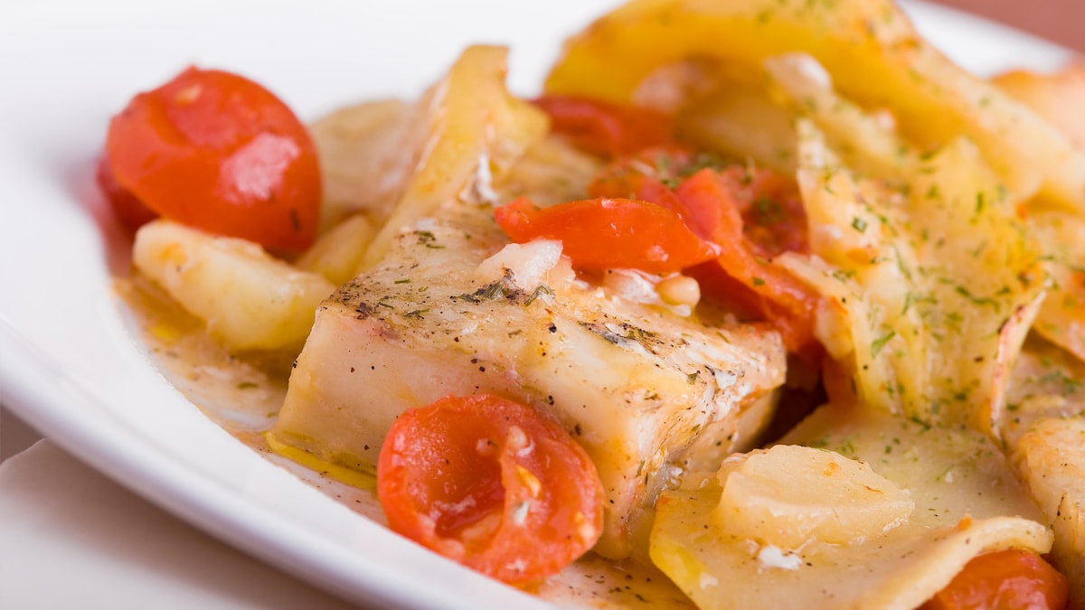 On voit un repas de poisson, de tomates et de pommes de terre, servi dans une assiette.
