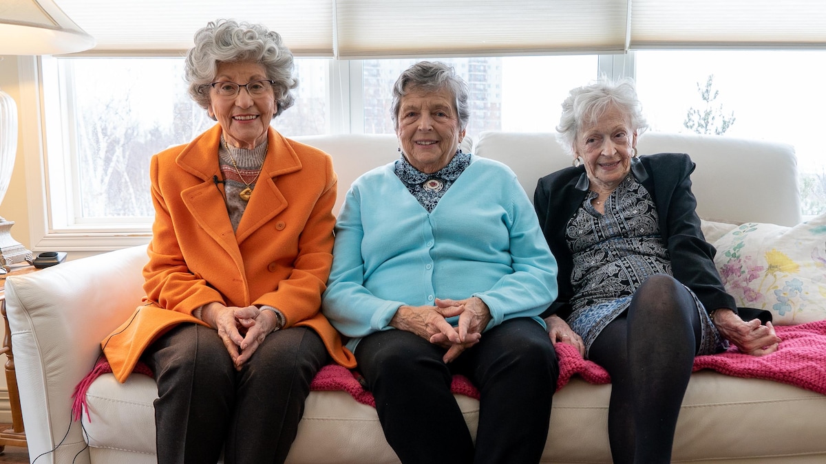 Trois dames assises sur un sofa, regardant la caméra en souriant.