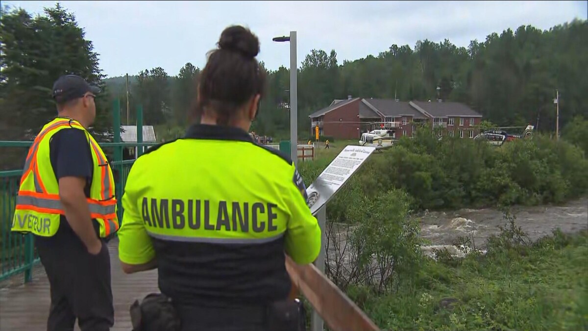 Des ambulanciers de dos avec deux hélicoptères de la Sûreté du Québec au sol.