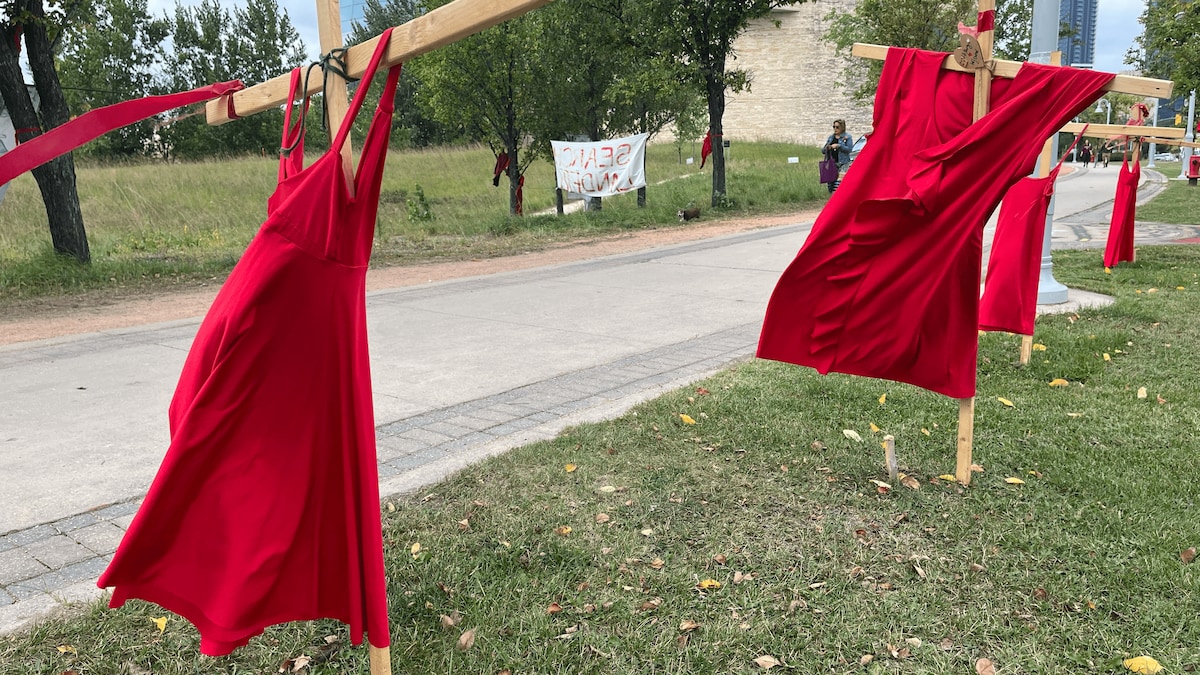 Des robes rouges sont accrochées à des croix de bois.