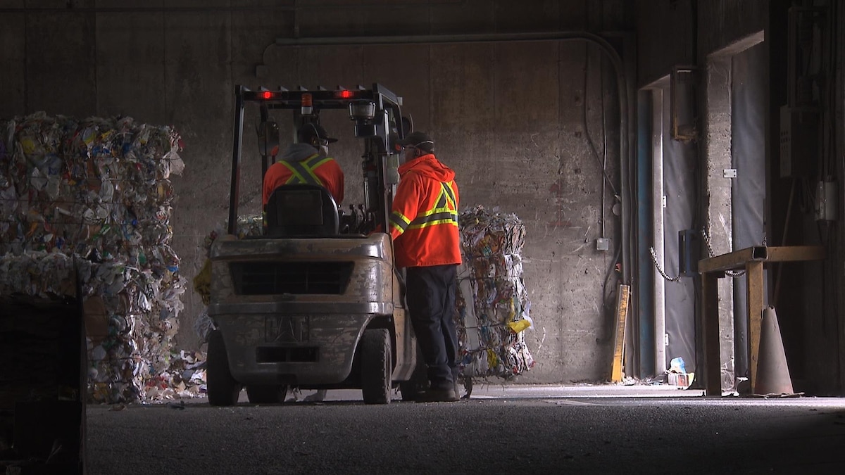 Des travailleurs du centre de tri de Montréal chargent des conteneurs de papier recyclé.