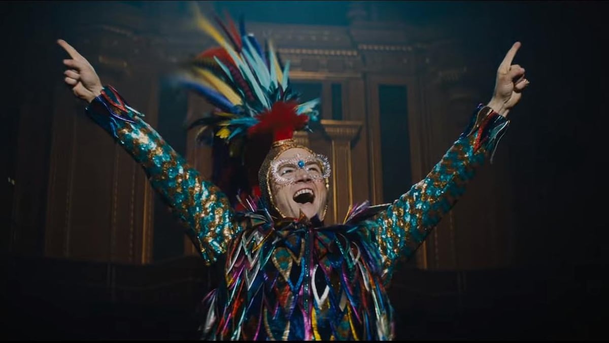 L'acteur Taron Egerton, qui incarne Elton John, a les bras levés en l'air et porte un costume multicolore couvert de fausses plumes.