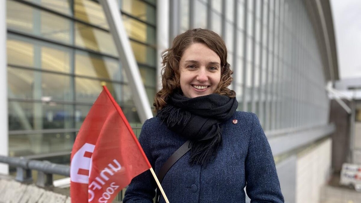 Roxanne Dubois se tient sur une passerelle de l'aéroport avec un drapeau avec le logo d'Unifor dans les mains.