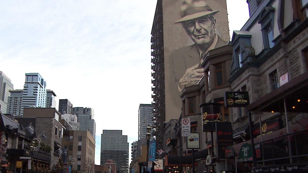 Des devantures de commerces rue Crescent, à Montréal, alors qu'on voit une murale de Leonard Cohen en arrière-plan.