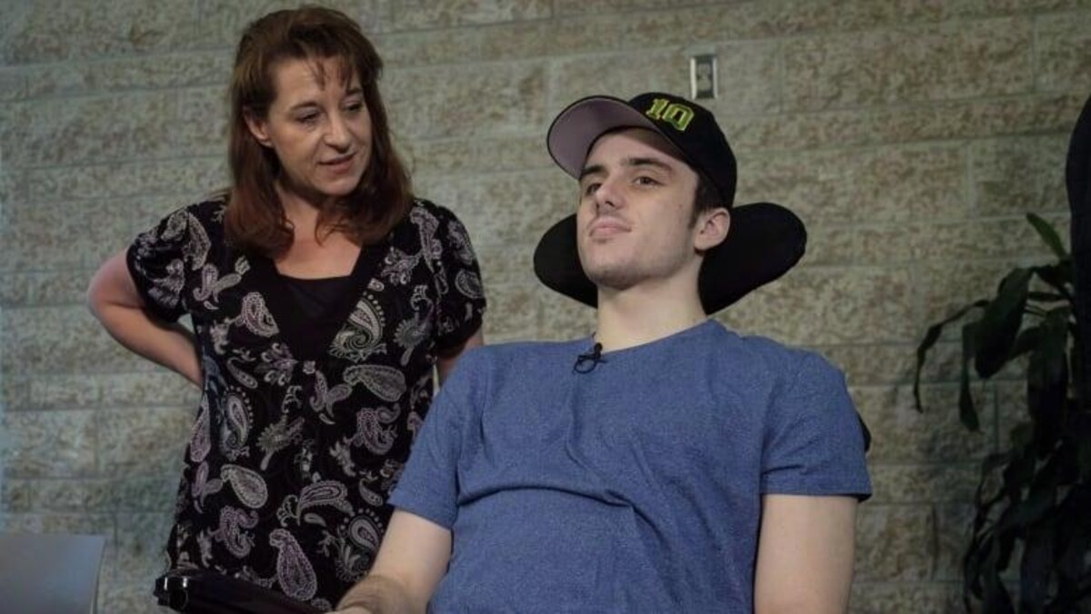 Un jeune homme est dans une chaise roulante. Sa mère se trouve à ses côtés.