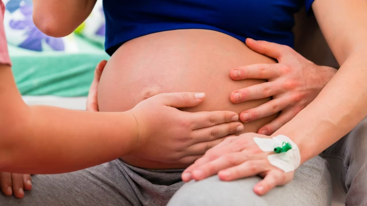 Des mains sont posées sur le ventre d'une femme enceinte.   