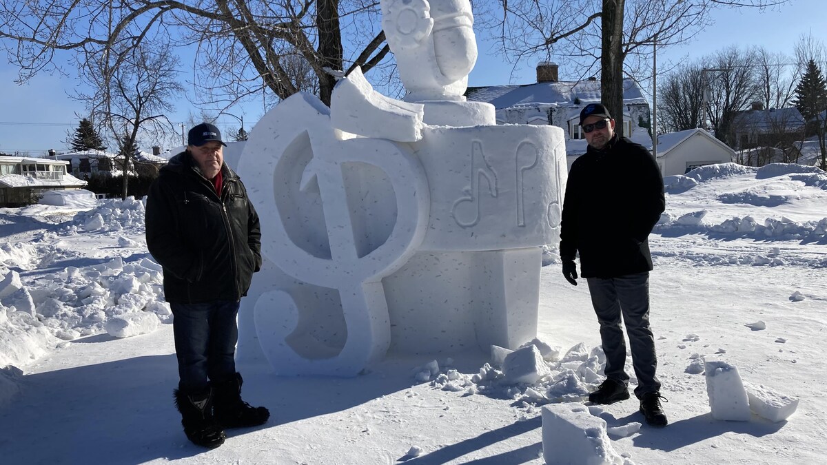 Deux hommes posent devant une sculpture de neige brisée.