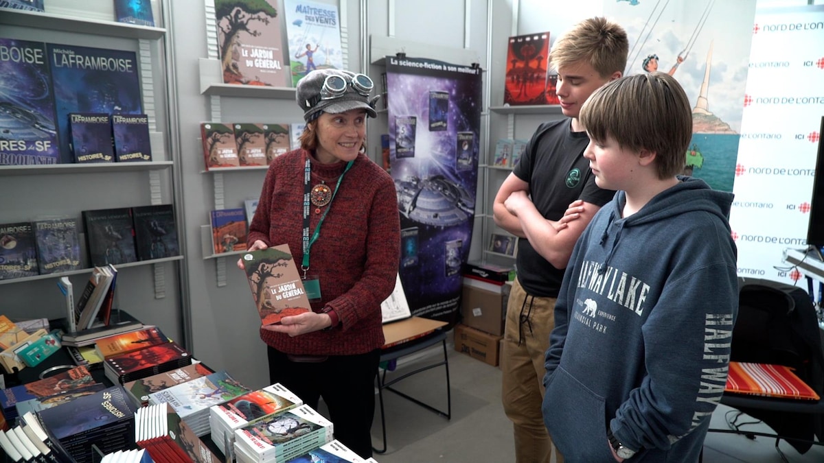 Une autrice tient son livre dans ses mains et le présente à deux jeunes élèves.