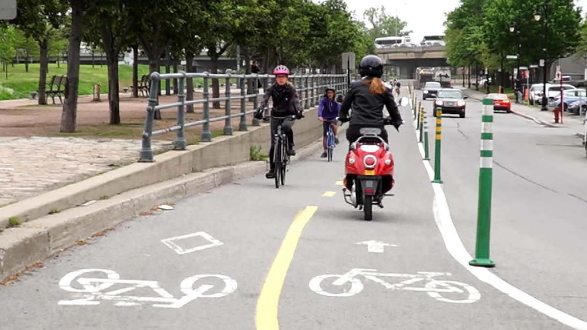 Une dame circule à scooter électrique sur une piste cyclable de Montréal. Elle croise des vélos. 