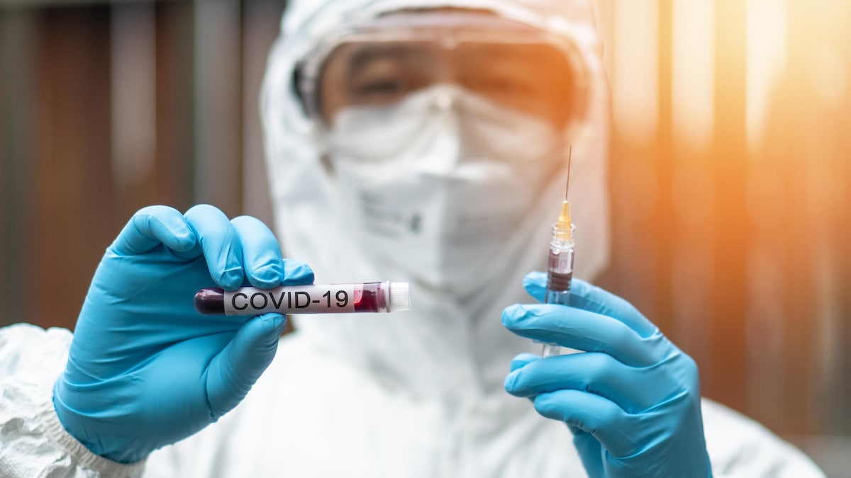 Un scientifique tient une seringue et une éprouvette sur laquelle il est écrit "COVID-19".
