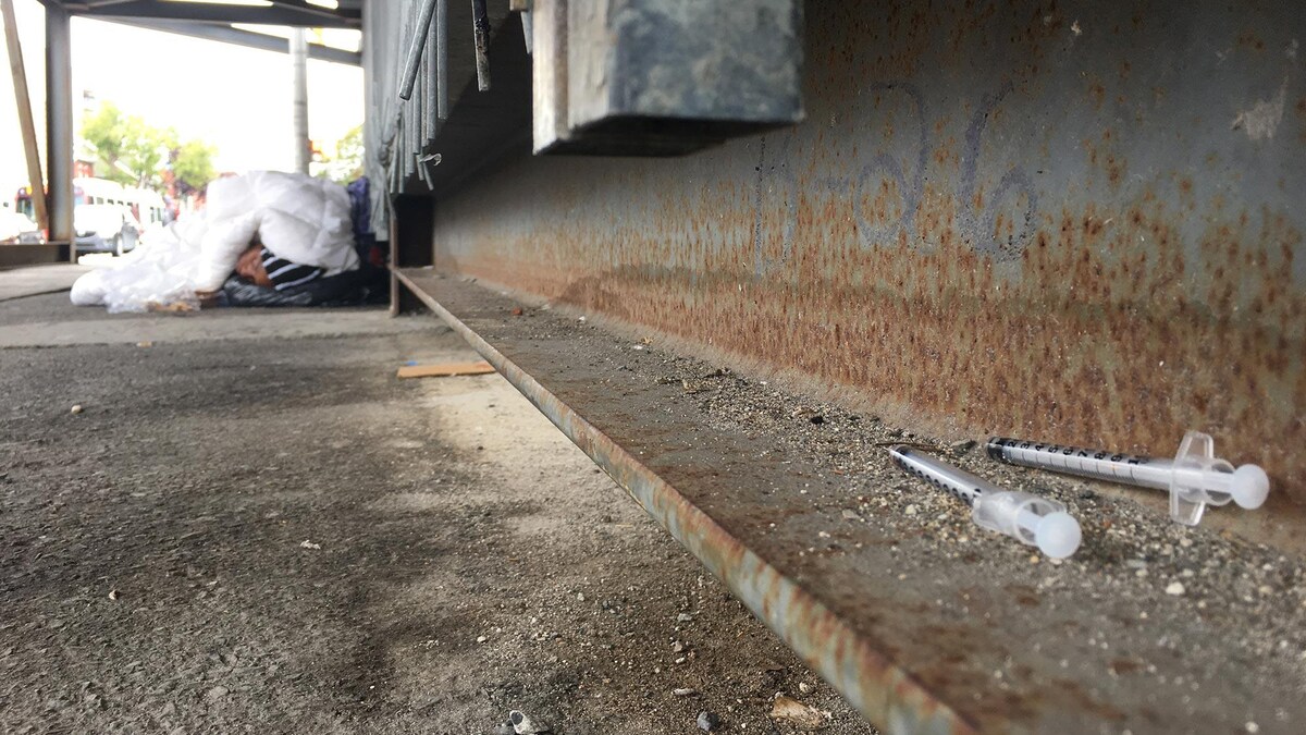 Des seringues souillées, sur le sol, près d'un sans-abri qui dort.