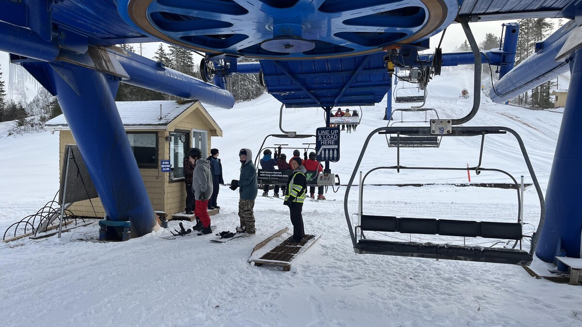 Des jeunes planchistes attendent le télésiège en bas de la montagne. D'autres sont déjà assis plus haut.