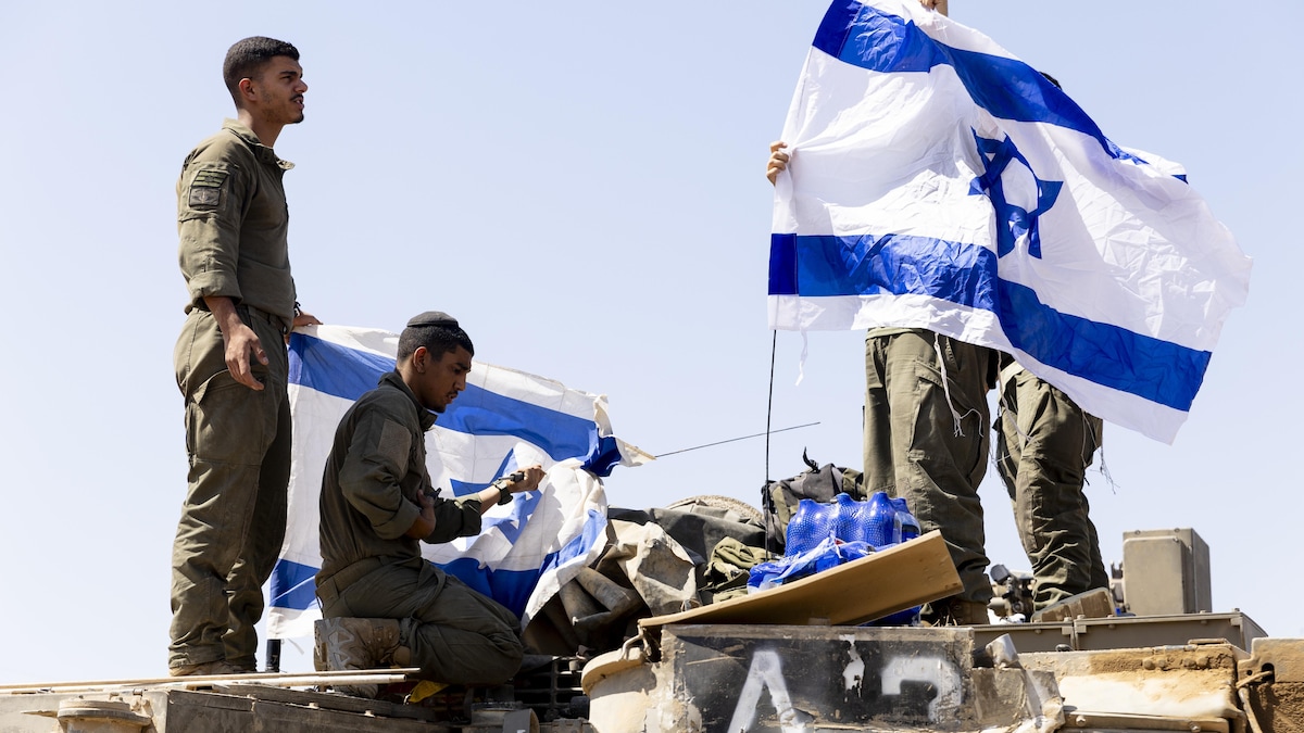 Des soldats israéliens accrochent des drapeaux israéliens à un véhicule blindé.