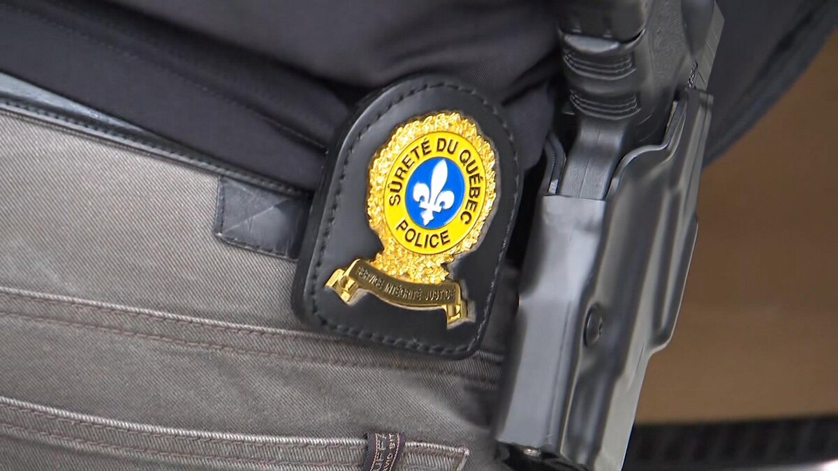 L'écusson de la Sûreté du Québec à la ceinture près d'une arme à feu.