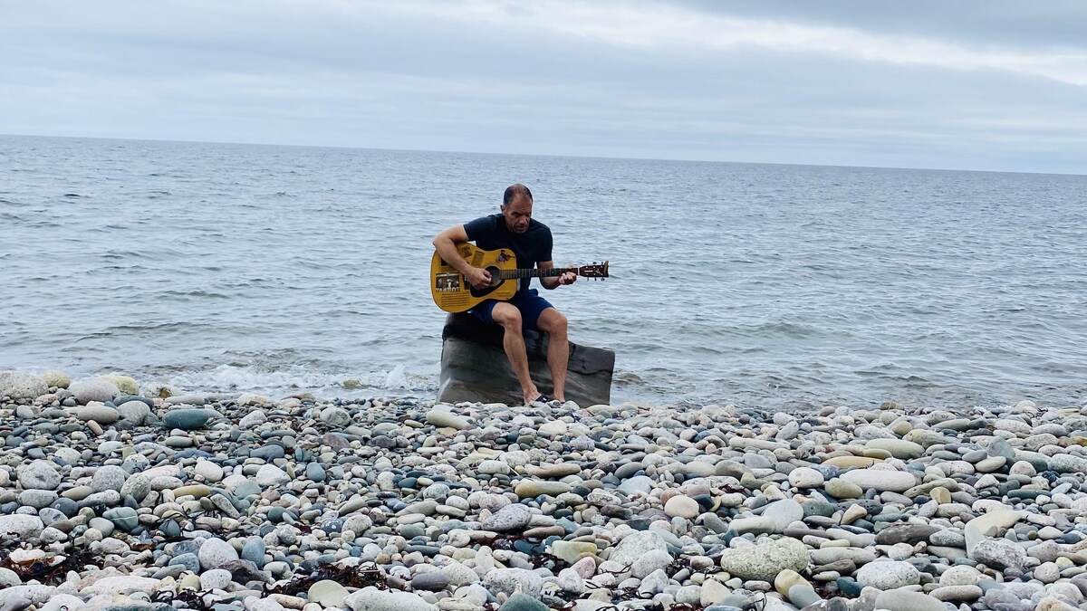Stéphane Doucet jouant de la guitare assis sur une roche.