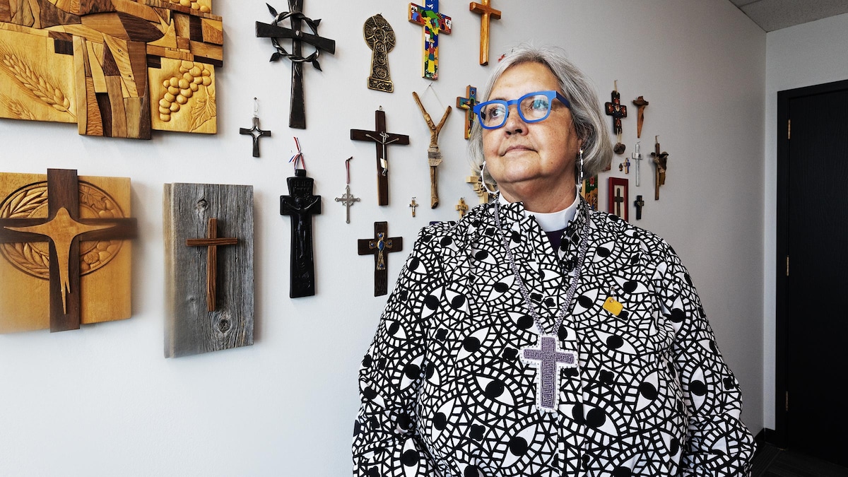 Une femme portant un crucifix de billes au cou devant un mur couvert de crucifix.