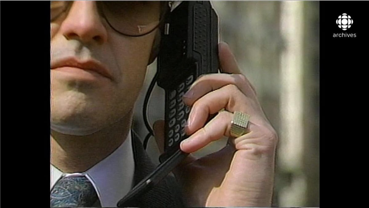 Homme en complet tenant un téléphone cellulaire à son oreille, avec une grosse bague en or à son auriculaire